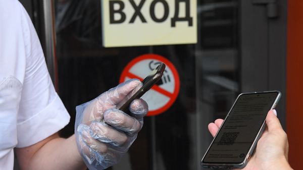 Посетитель показывает специальный QR-код на экране смартфона на входе в кафе