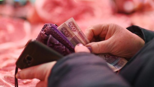 Покупатель достает деньги из кошелька у прилавка с мясом 