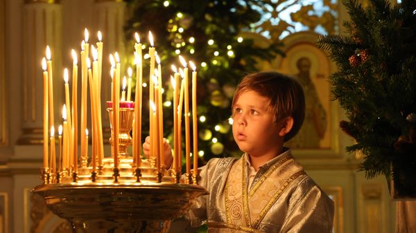 Мальчик зажигает свечу во время празднования православного Рождества в Русской православной церкви в Шардже