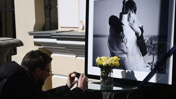Мужчина фотографирует цветы и портрет модельера возле дверей в Дом моды Валентина Юдашкина