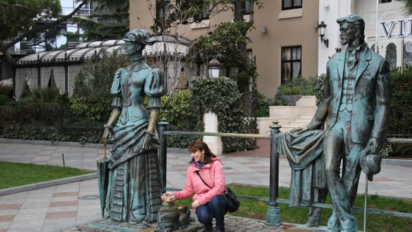 Женщина фотографируется с памятником Дама с собачкой на набережной Ялты Женщина фотографируется с памятником Дама с собачкой на набережной Ялты