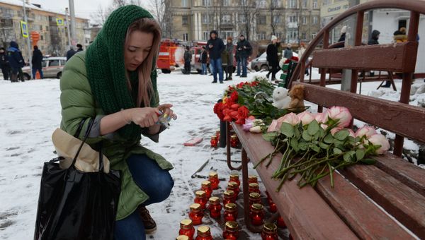 Женщина зажигает свечу возле здания торгового центра «Зимняя вишня» в Кемерово, где произошел пожар
