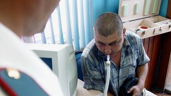 Сотрудник ГИБДД проверяет водителя автотранспорта новым прибором алкотестером на содержание алкоголя в крови.
