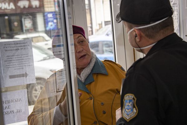 Охранник в маске объясняет пожилой посетительнице без маски, что по крайней мере неделю сюда приходить смысла нет.