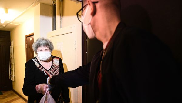 Волонтер штаба Мосволонтер передает женщине пакет с продуктовым заказом Волонтер штаба Мосволонтер передает женщине пакет с продуктовым заказом