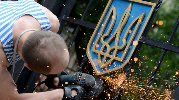 Боец ополчения Луганской народной республики срезает герб Украины с ворот здания областной администрации в Луганске